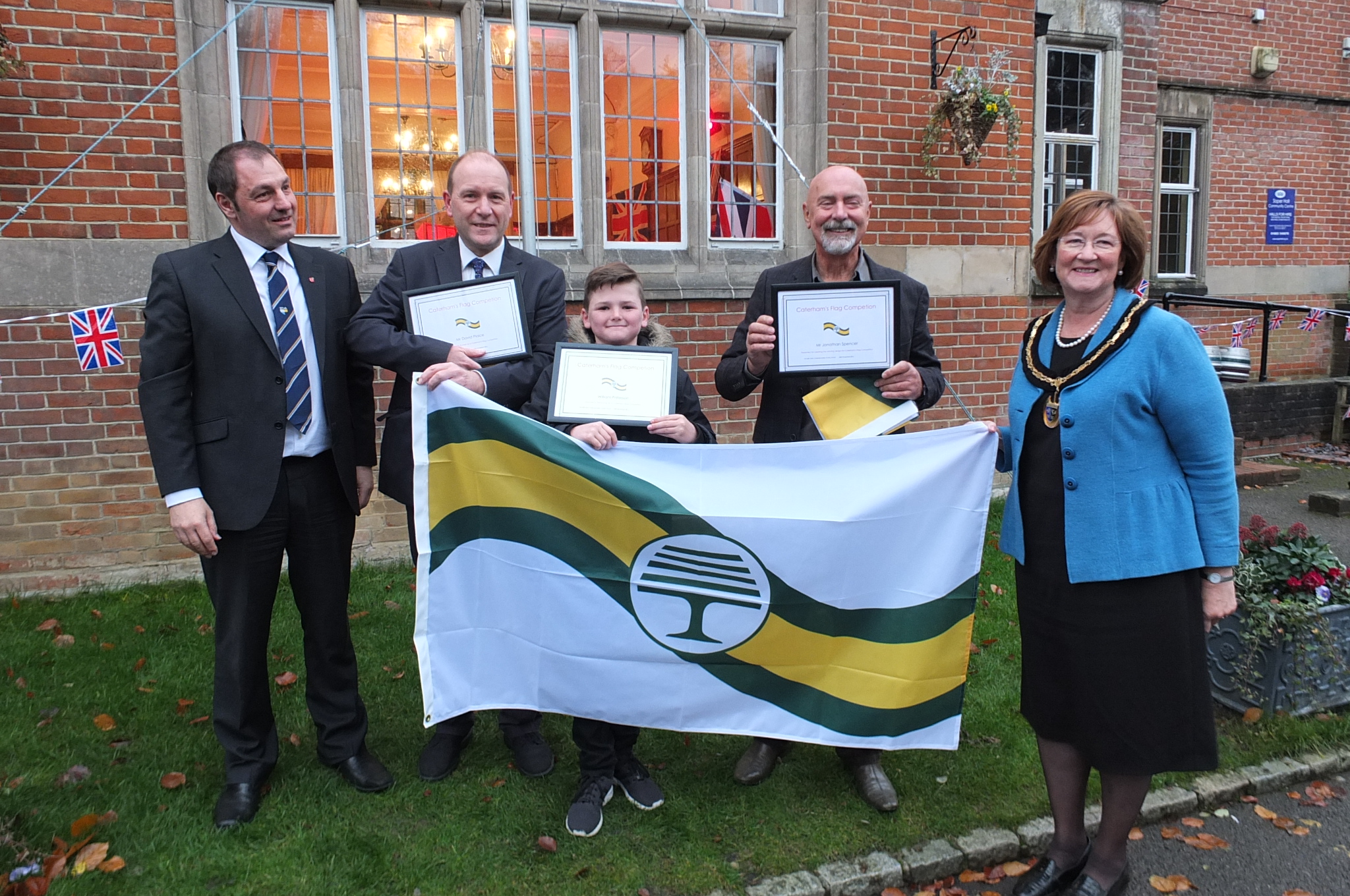 Photo caption:  From left:  Pete Dommett, David Plaice, William Paterson, Jonathan Spencer and the Chairman of Surrey County Council, Cllr. Sally Marks with the new Caterham Flag outside the Soper Hall.